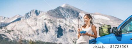 Travel driver woman eating food on camping road trip by her car. Panoramic banner of mountains landscape. Asian girl with lunchbox on autumn vacation Travel driver woman eating food on camping road trip by her car. Panoramic banner of mountains landscape. Asian girl with lunchbox on autumn vacation 82723503