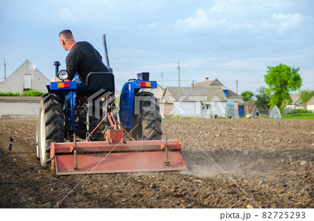 A farmer on a tractor cleans the field after harvest. Running a small agribusiness. Farm work. Softening soil before planting crops. Farming. Loosening, land cultivation. Mechanization in agriculture. A farmer on a tractor cleans the field after harvest. Running a small agribusiness. Farm work. Softening soil before planting crops. Farming. Loosening, land cultivation. Mechanization in agriculture. 82725293
