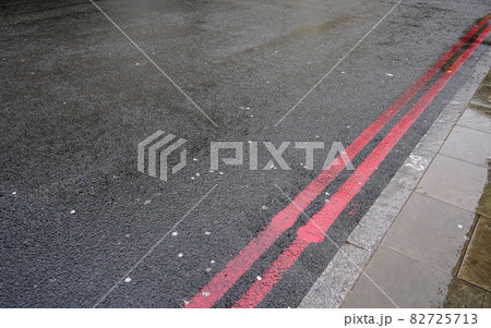 Double red line near curb on wet asphalt road. In London these indicate stopping forbidden any time, and are used instead of yellow lines sometimes. 82725713