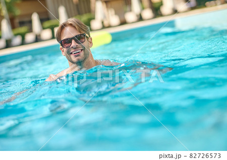 A young man in sunglasses swimming in a pool 82726573