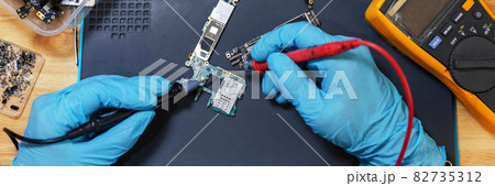 Phone repair concept a young electrical technician using an ammeter measuring the current in a circuit of an electronic device 82735312