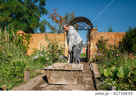 Eldery man kneads cement for pouring a garden path, garden construction work 82738639