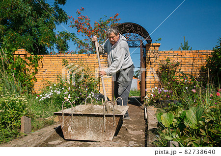 Eldery man kneads cement for pouring a garden path, garden construction work Eldery man kneads cement for pouring a garden path, garden construction work 82738640