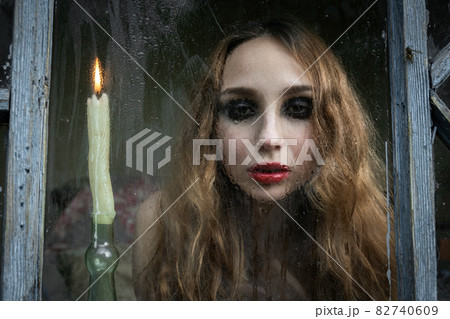 Beautiful sad young girl looking out the window with a candle 82740609