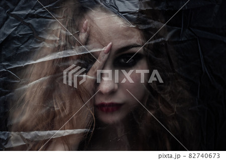Young beauty sad woman trapped behind a plastic sheet as protection against COVID-19. Nicely fits for book cover 82740673