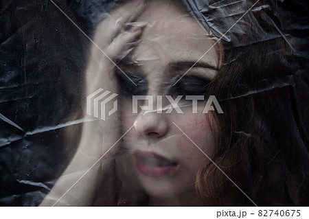 Young beauty sad woman trapped behind a plastic sheet as protection against COVID-19. Nicely fits for book cover 82740675