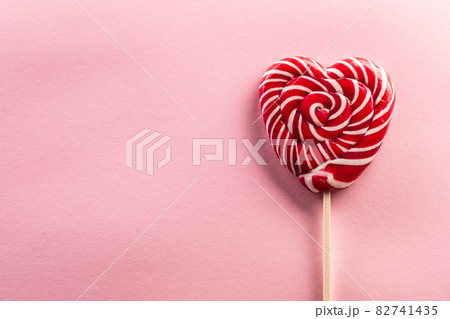 Delicious looking sweet heart-like lollipop stitched on a wooden stick with rose type in background 82741435