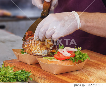 A chef prepares a burger for a customer. A man wearing white protective gloves picks up the burgers from the grill and and adds them to the burger bun. A chef prepares a burger for a customer. A man wearing white protective gloves picks up the burgers from the grill and and adds them to the burger bun. 82741990