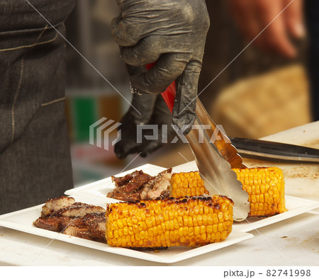 Chef prepares paper trays with grilled food, meat and corn for customers 82741998