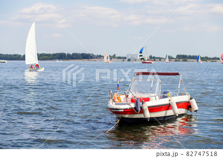 Motor boat moored to the shore. In the background are many yachts with sails. Summer is in full swing Motor boat moored to the shore. In the background are many yachts with sails. Summer is in full swing 82747518