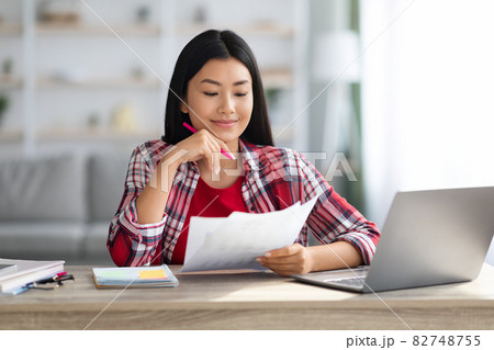 Home Office. Young Asian Female Sitting At Desk And Working With Papers Home Office. Young Asian Female Sitting At Desk And Working With Papers 82748755