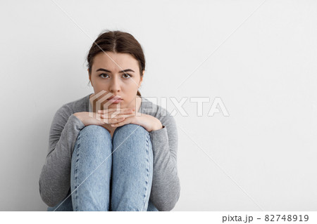 Scared sad worried millennial european woman sits on floor at home interior, on gray wall background 82748919