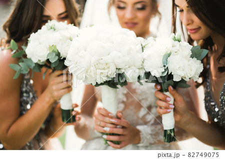 Bride with bridesmaids holding wonderful luxury wedding bouquet of different flowers on the wedding day 82749075
