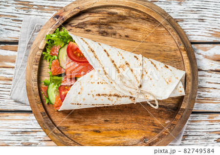 Wrap salmon sandwich, roll with fish and vegetables. White wooden background. Top view Wrap salmon sandwich, roll with fish and vegetables. White wooden background. Top view 82749584