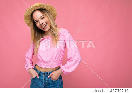 Portrait of young attractive smiling hipster blonde woman in stylish pink crop top and straw hat Portrait of young attractive smiling hipster blonde woman in stylish pink crop top and straw hat 82750216