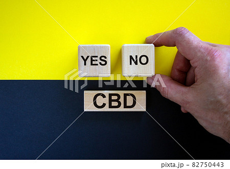 Man holds a cubes with word 'no'. Wooden cubes with word 'yes' and word 'plan'. Beautiful yellow and black background. Copy space. Concept of CBD legalization and use. 82750443