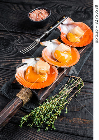 Scallops raw Shellfish on a wooden board with herbs. Black wooden background. Top view Scallops raw Shellfish on a wooden board with herbs. Black wooden background. Top view 82750589