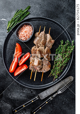 Roasted meat skewers shish kebab and vegetables on a plate. Black background. Top view Roasted meat skewers shish kebab and vegetables on a plate. Black background. Top view 82754175