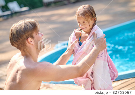 A young man wdrying his kid with a towel bear the pool 82755067