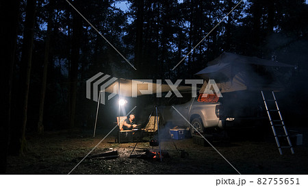 Happy hipster traveler people enjoying the alternative vacation - car with tent on the roof and alone man cooking in the forest. Adventure travel lifestyle wanderlust. Camping in the wilderness 82755651