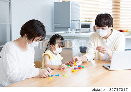 自宅のダイニングテーブルでマスクをして粘土で遊ぶ小学生の女の子とパパとママ 82757017