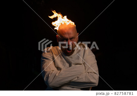 Bald man in a straitjacket with a burning head on a dark background. Bald man in a straitjacket with a burning head on a dark background. 82758781