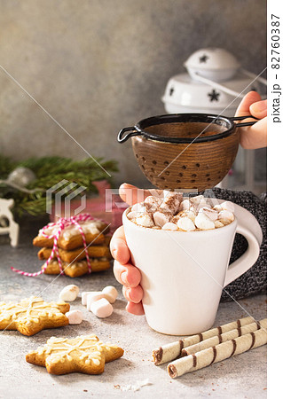 Female hands holding a cup of hot cocoa with marshmallows, Christmas sweets on a stone countertop. Copy space. Female hands holding a cup of hot cocoa with marshmallows, Christmas sweets on a stone countertop. Copy space. 82760387