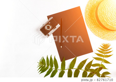 Straw hat with green leaves and old camera on white background, Summer background. Top view. Sun flare 82761710