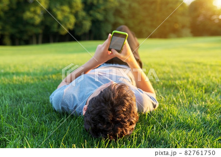 Guy teenager lying on grass with smartphone. Guy teenager lying on grass with smartphone. 82761750