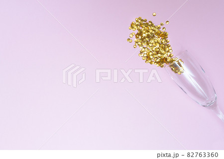Glass of champagne with loose sparkles on a pink background and place for text. Holiday and celebration concept. New Year. Copy space. 82763360