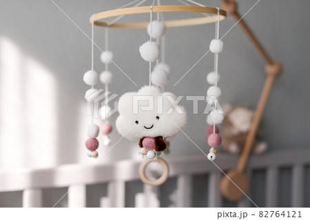Baby crib mobile with smiling clouds and snow. Kids handmade toys above the newborn crib. First baby eco-friendly toys made from felt and wood hanging in light room 82764121