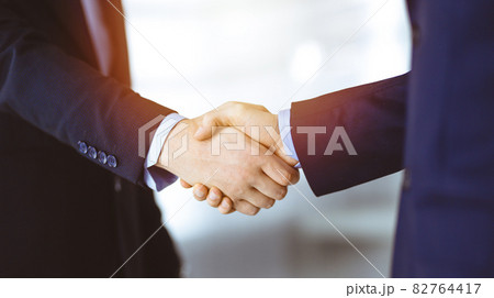 Business people shaking hands, close-up. Group of unknown businessmen standing in a sunny modern office. Teamwork, partnership and handshake concept 82764417