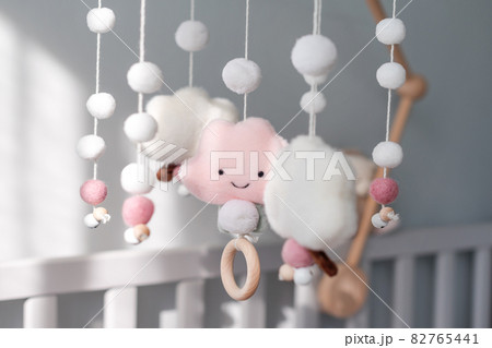 Baby crib mobile with smiling clouds and snow. Kids handmade toys above the newborn crib. First baby eco-friendly toys made from felt and wood hanging in light room 82765441