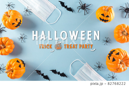 Halloween decorations made from pumpkin, paper bats and surgical face mask on pastel blue background. Flat lay, top view of Halloween celebration during covid-19 pandemic situation. 82768222