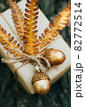 A gift wrapped in craft paper and decorated with dried fern leaves and glass acorns. 82772514