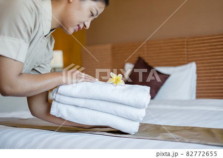 A hotel maid stacked towels on the bed and placed flowers on the towels in a hotel room 82772655