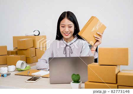 Young Asian woman business owner with many parcel boxes on the table happy online sales job, use your laptop, get an order from customers, take notes, and make arrangements for delivery by post Young Asian woman business owner with many parcel boxes on the table happy online sales job, use your laptop, get an order from customers, take notes, and make arrangements for delivery by post 82773146