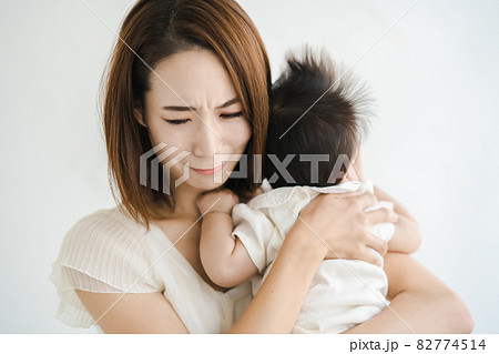 赤ちゃんを抱えて、疲れた表情をするお母さん 赤ちゃんを抱えて、疲れた表情をするお母さん 82774514
