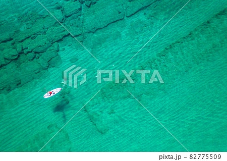 Alone man rowing on SUP board on aquamarine, blue sea water with coral in lagoon. Aerial top view paddleboard. Surfing 82775509