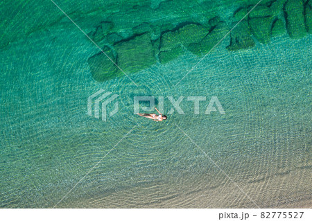 Young woman in a swimsuit lying on sea water on the beach. View from above. Top, drone view Young woman in a swimsuit lying on sea water on the beach. View from above. Top, drone view 82775527