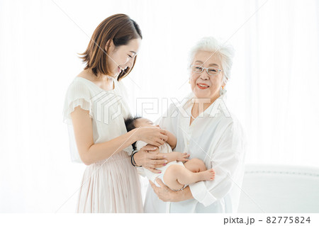 赤ちゃんを抱っこするシニア女性と見守る女性たち 82775824