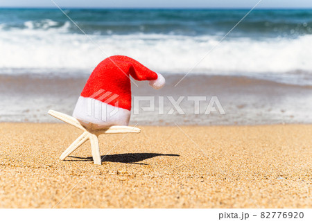 Christmas santa claus hat on starfish tourist on sand beach with sea water background. New year vacation concept Christmas santa claus hat on starfish tourist on sand beach with sea water background. New year vacation concept 82776920