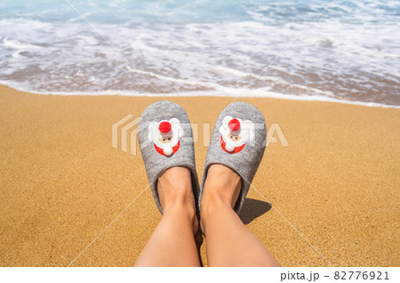 Christmas sea holiday. Woman in santa slippers relaxing on paradise beach island with waves. New year 82776921