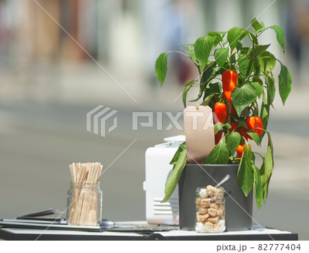 Small shrub with red peppers and jar of cane and white cubes sugar and other cafe equipment as an attraction of the adjacent restaurant and cafe. Blurred street in background. 82777404