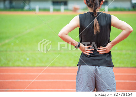 Back view of young runner woman suffering from Backache or Sore waist after running in the running track in stadium. Conceptual of woman suffering painful from sport workout. 82778154