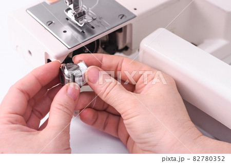 The seamstress inserts the spool into the bobbin of the sewing machine. metal cap in the hands of a dressmaker close-up. 82780352