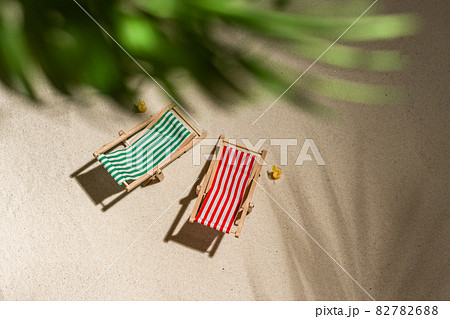 Aerial view two deck chair, glass of juice, flip flops on sand through the branches of palm and shadow palm tree. Travel, holiday, summertime, romantic concept. Top view. Aerial view two deck chair, glass of juice, flip flops on sand through the branches of palm and shadow palm tree. Travel, holiday, summertime, romantic concept. Top view. 82782688