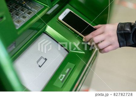 Woman withdrawing money from atm with a mobile phone a NFC terminal 82782728