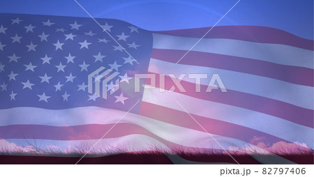 Composition of american flag billowing over grassy horizon and blue sky 82797406