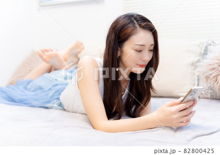 リラックスしてベッドでスマホを見る女性 82800425